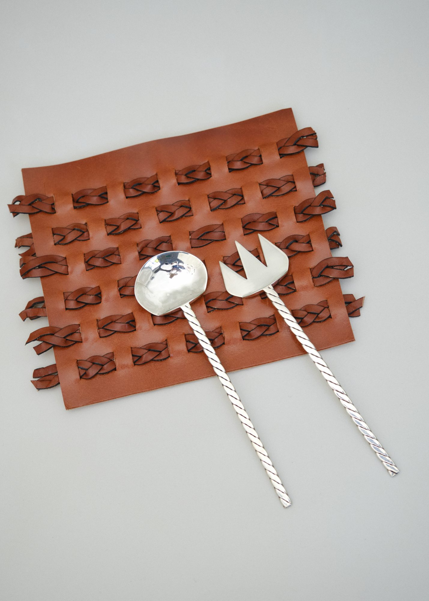 Silver serving cutlery with braided handles on leather weave